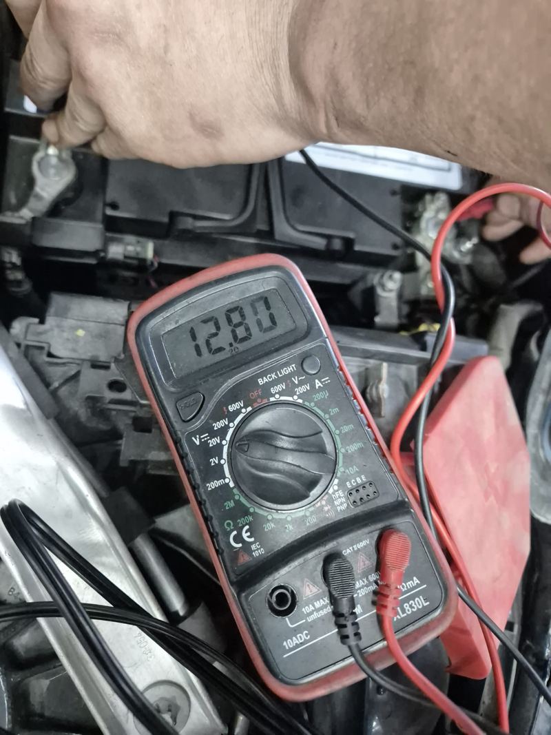 Multimeter on a car battery showing 12.80 volts
